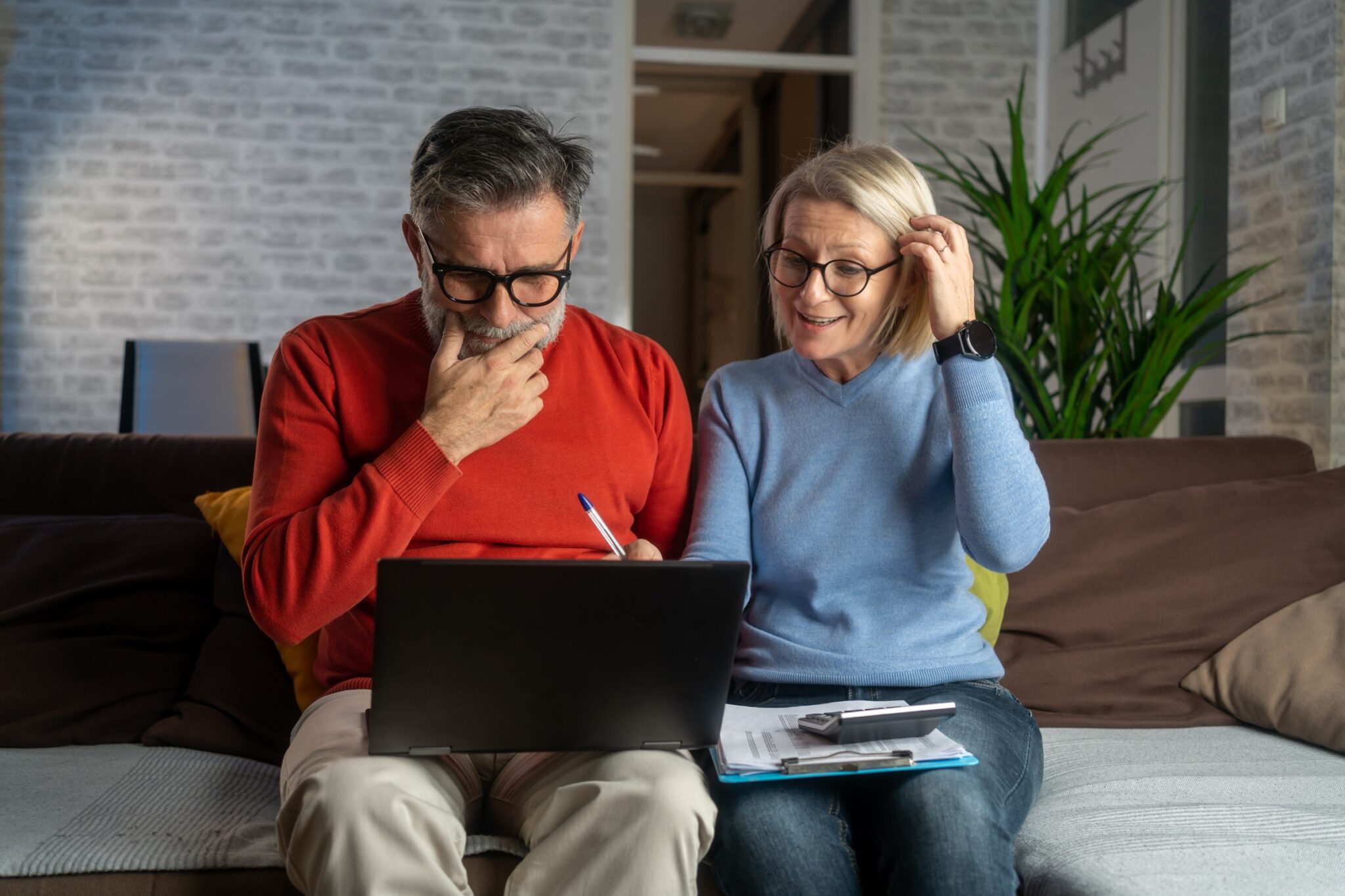 Elderly couple using laptop on sofa.